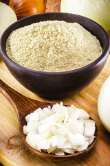 wooden spoon with sliced ​​onion and crushed into pieces to be used as seasoning, with powdered onion in the background, rustic kitchen