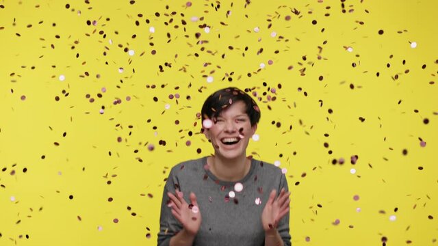 Color of the year 2021. Ultimate Gray and illuminating. Happy excited beautiful woman wearing gray sweatshirt jumping, clapping hands, celebrating victory under falling confetti on yellow background