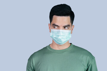 Stressful COVID-19 Coronavirus portrait handsome young asian .man wearing green shirt and mask protection from covid 19 isolated on gray background in studio. Asian man people. COVID-19 concept.