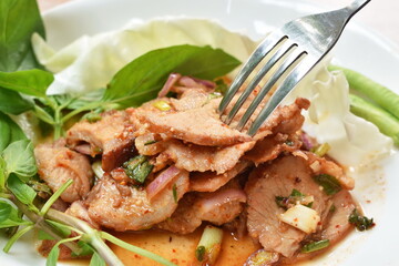 spicy roasted pork Thai salad eat with fresh basil leaf and cabbage on plate stabbing by silver fork