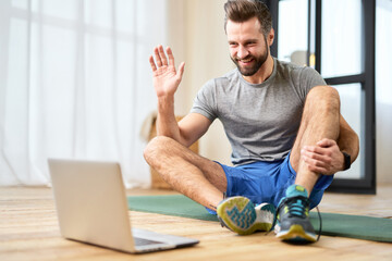 Athletic young man using laptop for online communication at home