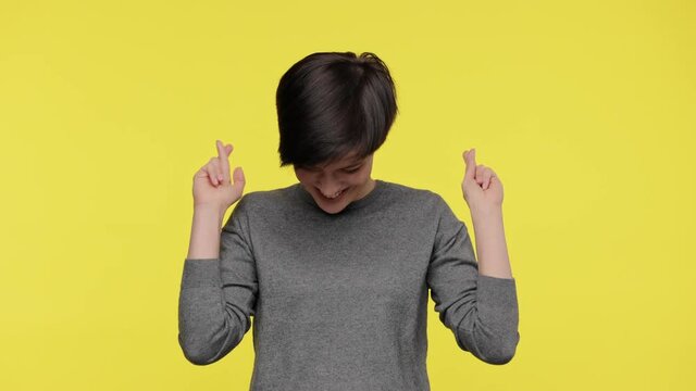 Color of the year 2021. Ultimate Gray and illuminating. Young beautiful woman wearing gray sweatshirt praying for good luck, cross fingers and making a wish isolated on yellow background