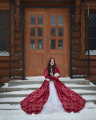 Fototapeta premium A woman in a red Russian dress and white mittens on the steps of the church