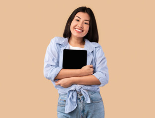 Excited asian woman hugging tablet at studio