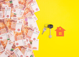 Fototapeta na wymiar Five thousand Russian rubles banknotes on a yellow background and the keys to the apartment and a red paper house. The concept of buying a home, mortgage. Top view, free space for text