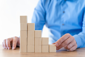 Businessman hand arranging wooden blocks in an upward stepping stair.  Concept for growth, success, investment strategy.