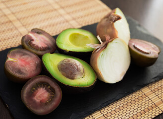 vegetables black tomatoes, avocado and onions on black stone board