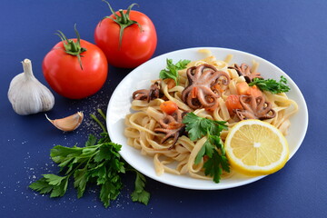 pasta with seafood and tomatoes on the white plate on the dark blue background