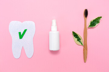 Concept of eco friendly hygiene products. A bamboo toothbrush with green leafs, a mouth freshener and a tooth cut out out of felt with a sign ok. Pink background. Flat lay