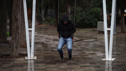 Lonely man in the park swinging on a swing. A sad man in depression is lonely swinging on a swing in an empty winter park.