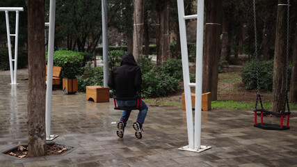 Lonely man in the park swinging on a swing. A sad man in depression is lonely swinging on a swing...