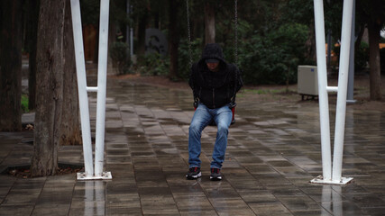 Lonely man in the park swinging on a swing. A sad man in depression is lonely swinging on a swing in an empty winter park.