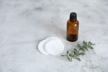 A brown glass bottle, cotton swabs, a green twig on a gray table. Cosmetics concept