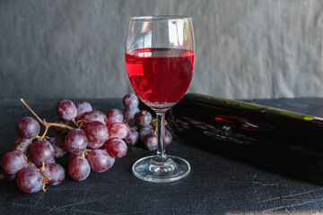 Red wine and wine bottle with grapes on black background