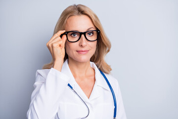 Photo of mature beautiful serious professional woman doctor with glasses and stethoscope isolated on grey color background