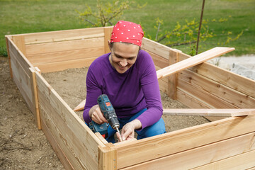 Woman screwing wooden frame for a raised garden bed.