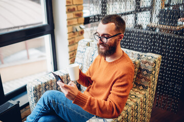 Cheerful man dialing number on smartphone in cafeteria
