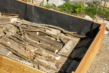 Branches and logs in a new wooden frame for a raised garden bed.