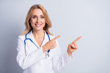 Photo of mature happy smiling charming doctor woman point fingers copyspace recommend isolated on grey color background