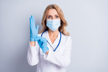 Portrait of pretty lady put on gloves wear face safe medical healthcare mask isolated on grey color background