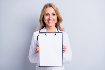 Photo of mature charming smiling doctor woman hold showing organizer check list isolated on grey...