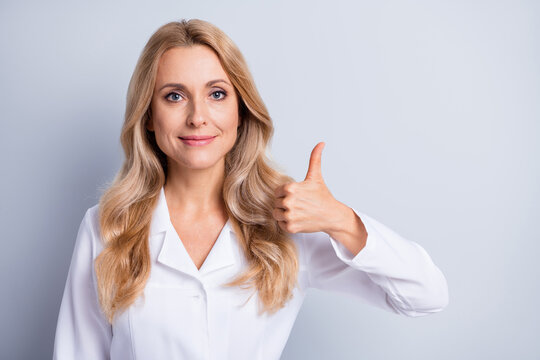 Photo of mature beautiful lovely pretty smiling woman doctor showing thumb-up isolated on grey color background