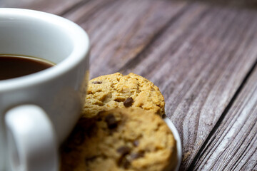 chocolate chip cookies next to a cup of coffee on a saucer on a rustic wooden table