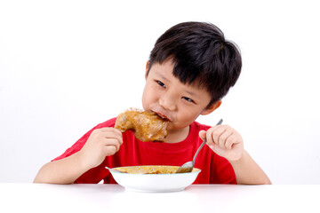 Portrait of cute little Asian boy enjoying eating chicken drumstick with noodles at home, isolated on white background.
