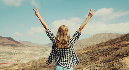 Rear view, happy young woman raising her hands up on a hiking trail on top of the mountain, view...