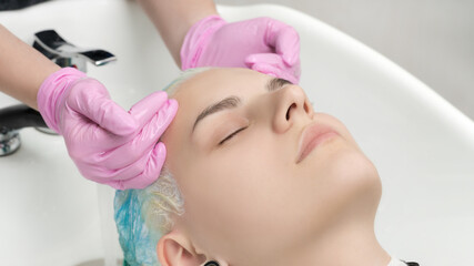 Hairstylist hands in pink gloves washing emerald hair color in professional beauty salon. Head of young woman with closed eyes in special sink hair salon.
