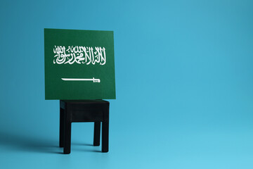 National flag of Saudi Arabia on a black chair, light blue background. Communication and dialog concept.