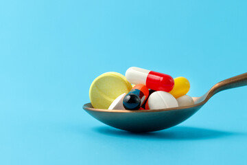 Fototapeta premium A spoonful of medicine pills and capsules on blue background.