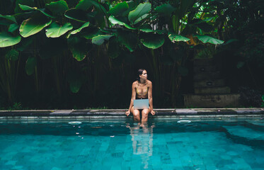 Lonely female in swimsuit using laptop in pool