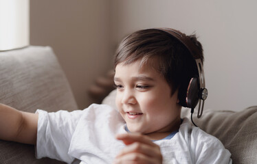 Close up Happy kid with smiling face,  Head shot positive child wearing headphone listening music in retro filter, Yong boy siting on sofa having fun or relaxing at home on weekend.