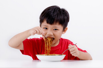 Cute little Asian boy enjoying eating noodles at home, isolated on white background