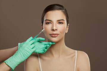 Beautiful woman face with syringe injection on brown background. Cosmetology and aesthetic surgery...