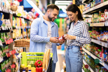 Young couple with the cart choosing products in supermarket