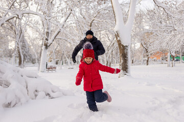 A handsome young Caucasian with a daughter in a red jacket and a knitted hat is running in the park in winter. Family vacation concept while traveling.