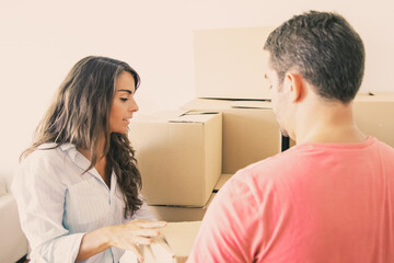 Obraz premium Man and woman carrying carton boxes among packages in new apartment. Transportation service or property buying concept