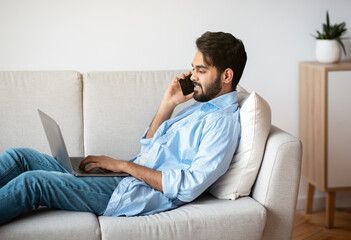 Freelance. Handsome Arab Man Using Laptop And Talking On Cellphone At Home