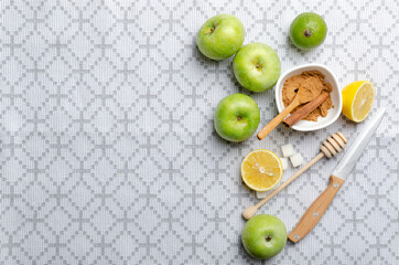 Top view of sweet green apples, lime and lemon, knife, sugar, honey comb on the kitchen tablecloth. Empty space
