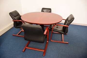 Four empty leather office chairs sit around a round table.