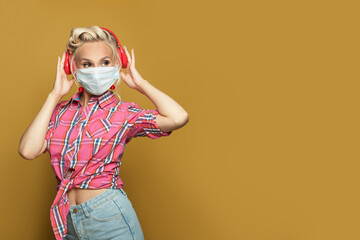 Pinup woman in medical protective mask listening music with headphones on yellow banner background