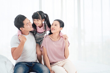 Fototapeta premium Happy Asian family (mother, father, child daughter) playing together on bed while smile in bedroom at home.