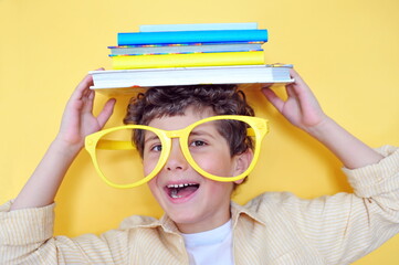Cute little boy holding many books on his head and smiling. Education background.
