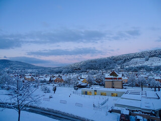 Panoramic view of the snowy village of Buhl, in Haut-Rhin, Alsace, France, at sunset, with forest and mountains in the background