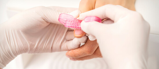 Closeup of manicurist is brushing dust with a pink plastic brush from female fingernails in a nail salon