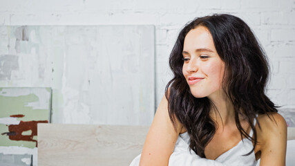 young brunette woman smiling while sitting in bedroom