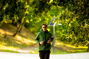 Athletic young man running while doing workout in sunny green park