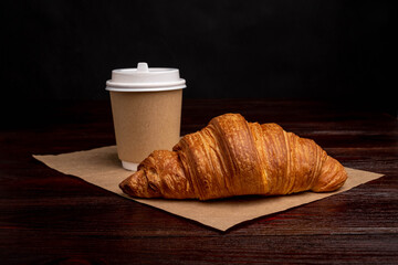 Croissant with coffee to go in a paper cup, take away breakfast